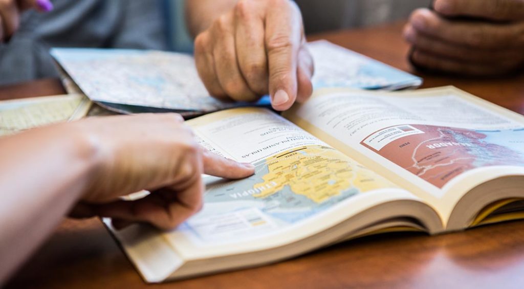 Decorative header: Map book open on a table, two people pointing at the page.