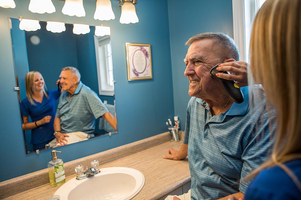 Caregiver helping shave elderly mans face