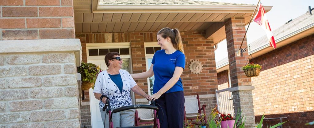 Nurse helping an elderly woman walking down her front veranda